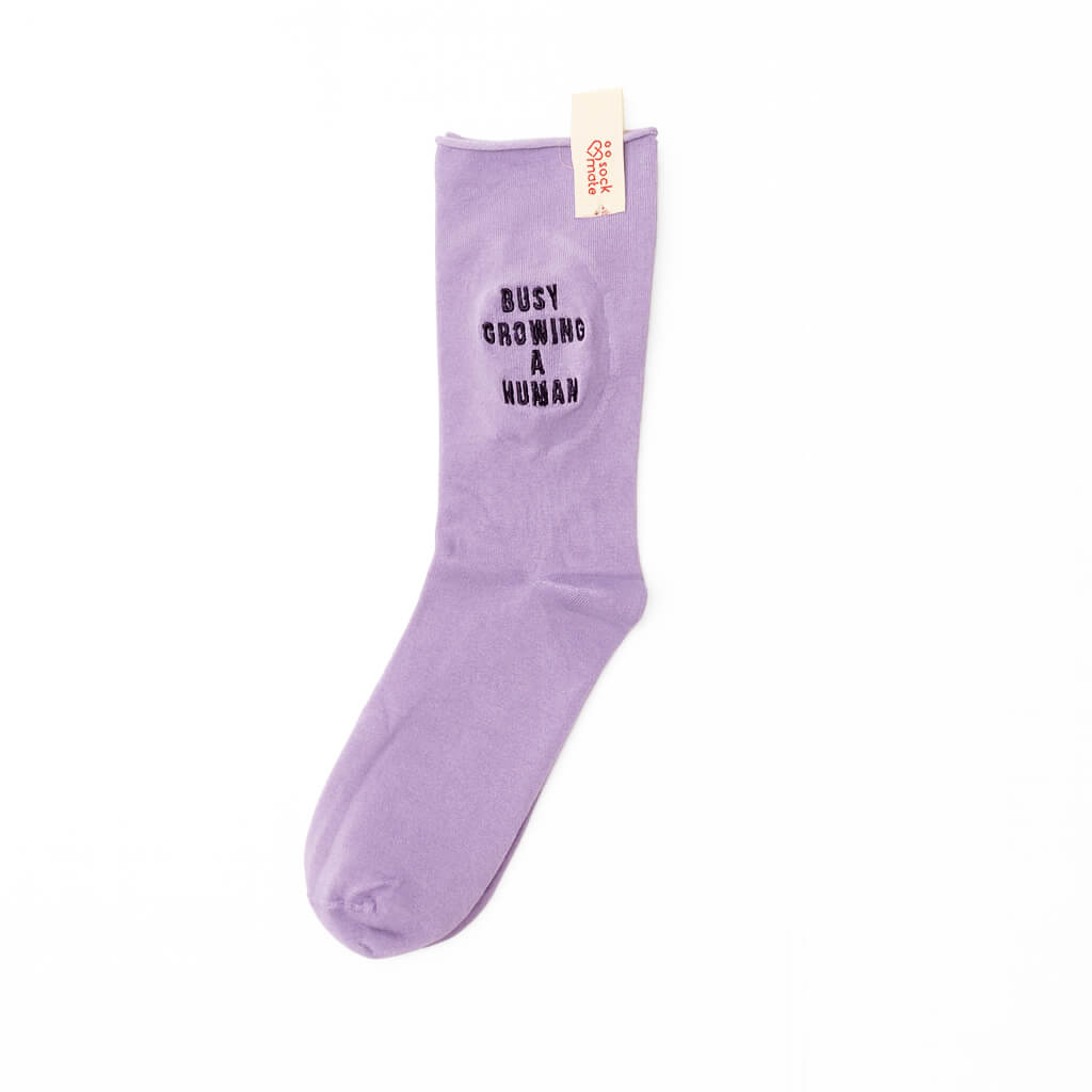 Single lilac sock with “Busy Growing a Human” embroidery, shown with Sockmate brand tag attached at the cuff.