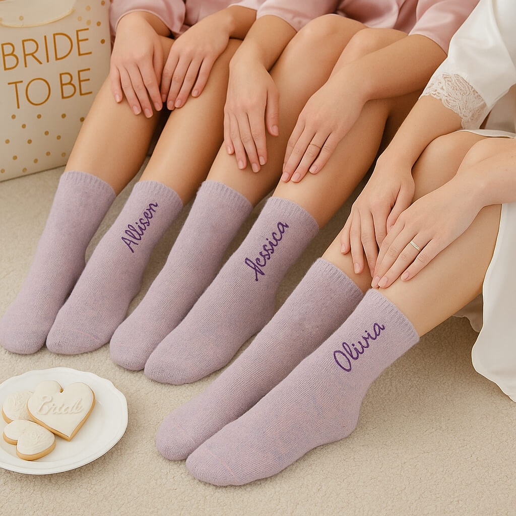 Bridesmaids sitting in blush robes wearing personalized lilac fuzzy socks with embroidered names, matching cozy bridal morning setting.