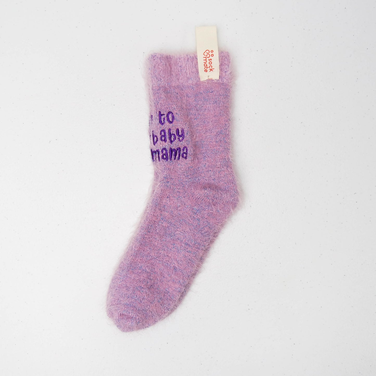 Single fuzzy lilac sock with purple embroidered text “to baby mama,” displayed flat with Sockmate brand tag attached at the cuff.