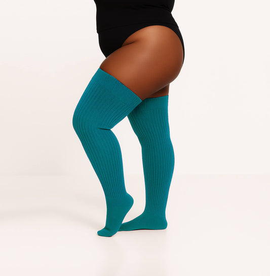 a woman wears teal color plus size thigh high socks and lay down on red couch. this over knee socks makes her cozy and sexy