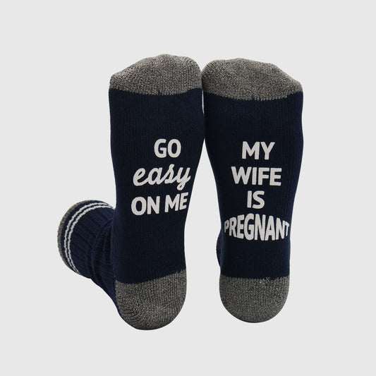 socks expressing a humorous and supportive sentiment for partners of pregnant women, reminding others to be mindful and understanding with the phrases 'GO EASY ON ME' and 'MY WIFE IS PREGNANT.
