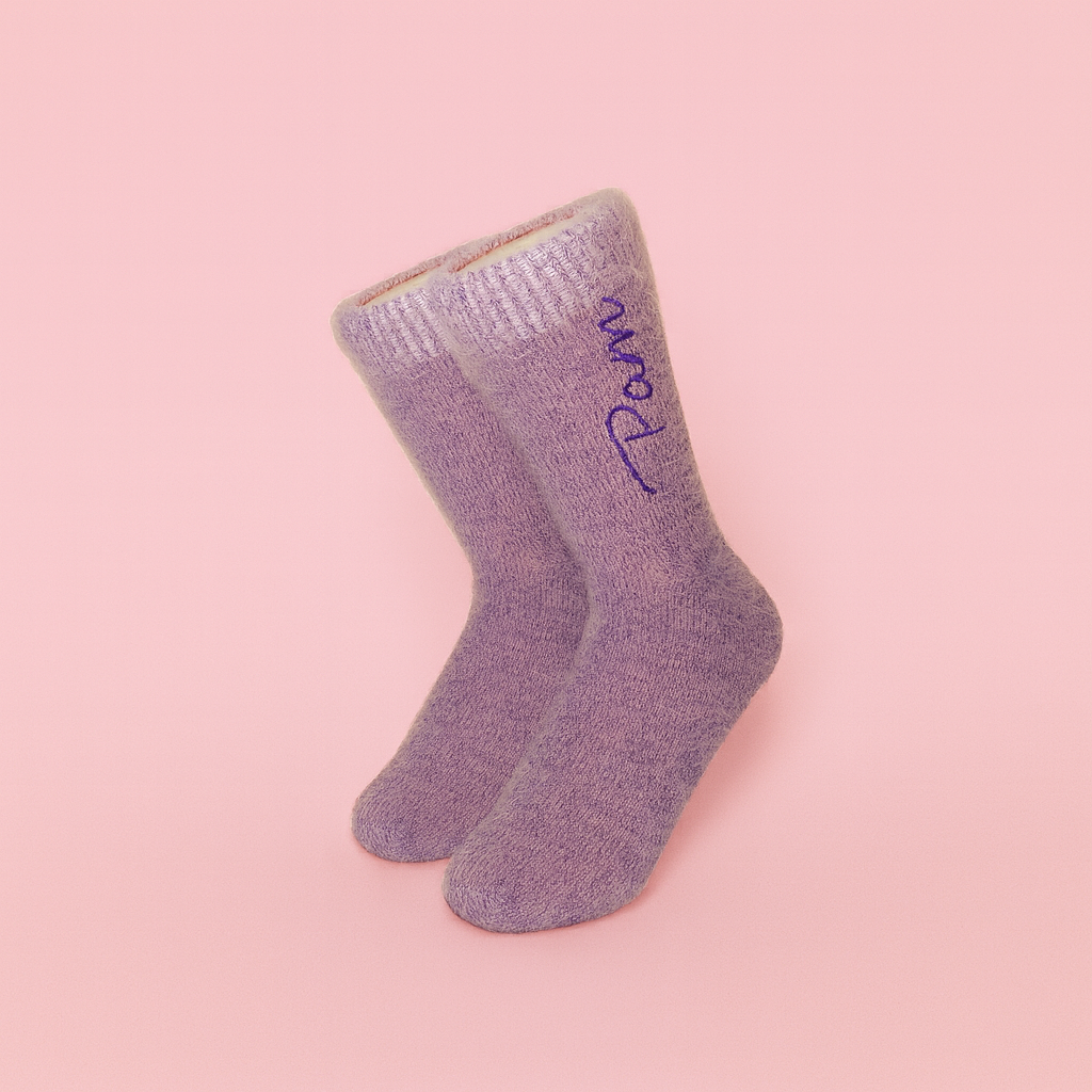 Pair of lilac glitter socks with “Pam” embroidery standing upright against pastel pink background, minimalist Sockmate product photo.