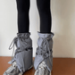 A person wearing black leggings and gray quilted puffy boot covers over sneakers, tied with adjustable laces, standing indoors against a plain wall.