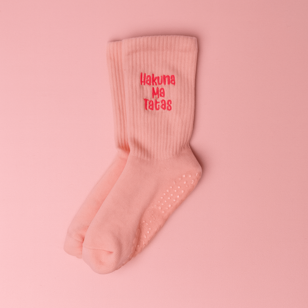 Light pink ribbed grip socks displayed on a matching pink background, embroidered in bright pink text that reads “Hakuna Ma Tatas.” The socks feature silicone grips on the soles for added traction.
