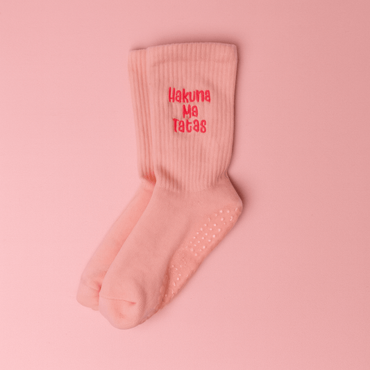 Light pink ribbed grip socks displayed on a matching pink background, embroidered in bright pink text that reads “Hakuna Ma Tatas.” The socks feature silicone grips on the soles for added traction.