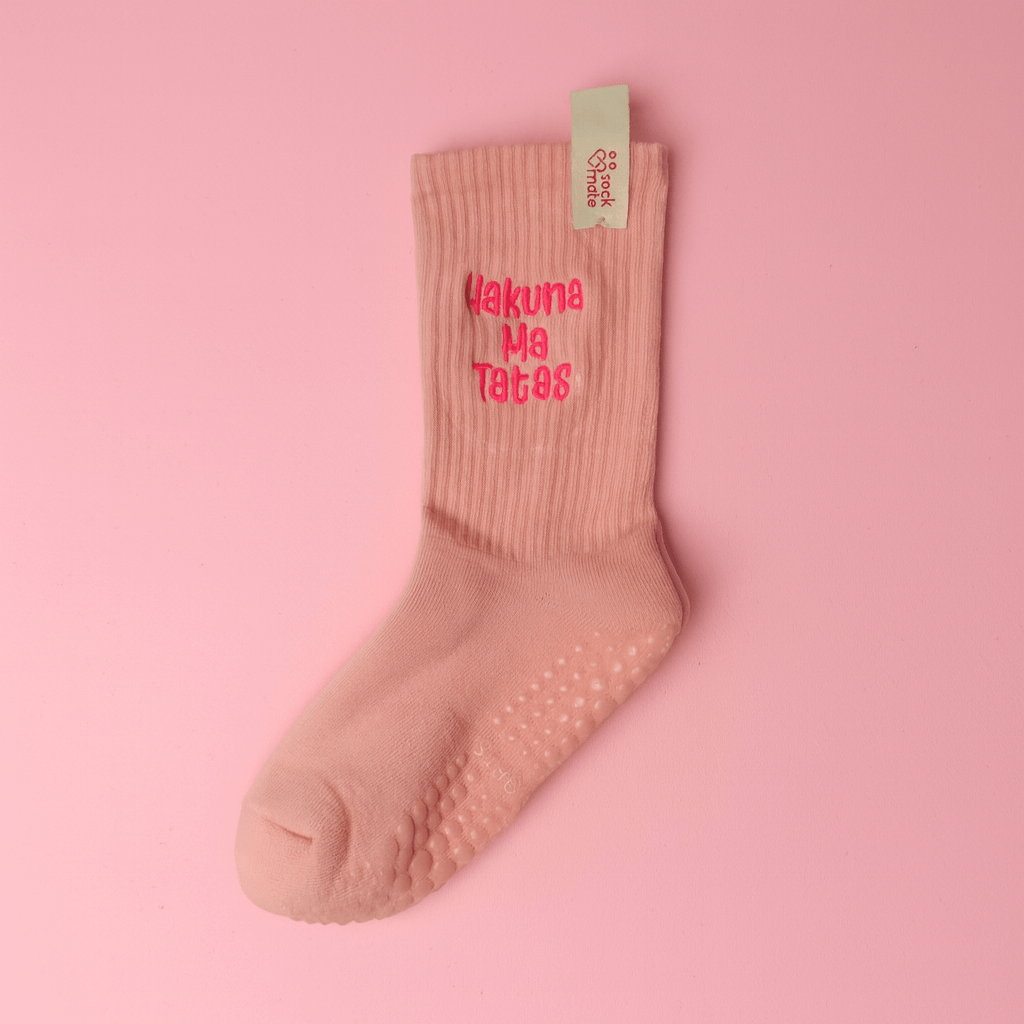 Single light pink ribbed grip sock with bright pink “Hakuna Ma Tatas” embroidery, laid flat on a pink background. The top includes a beige Sockmate tag with a heart logo, highlighting the brand detail.