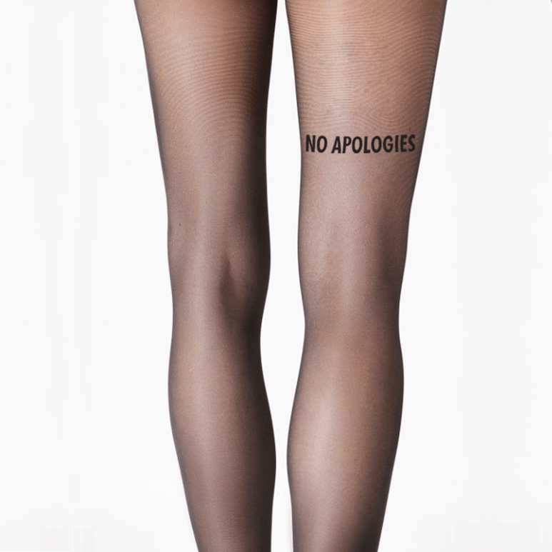 Black sheer tights worn on legs, featuring bold black text reading “NO APOLOGIES” printed on the right thigh against a clean white background.