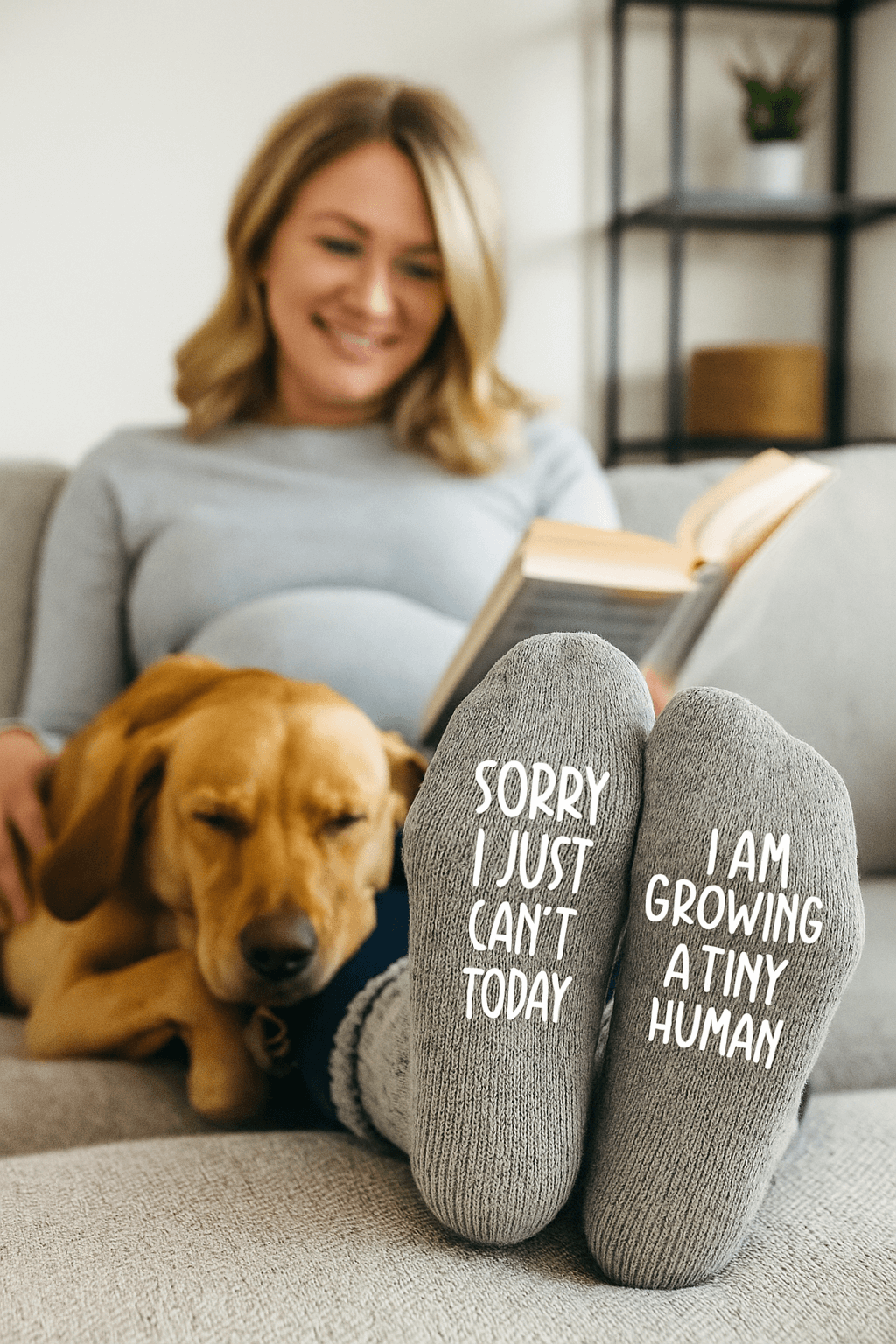 Woman sitting on a couch with a dog, wearing socks with humorous text "sorry I just can't today, i am growing a tiny human", in a cozy living room setting.