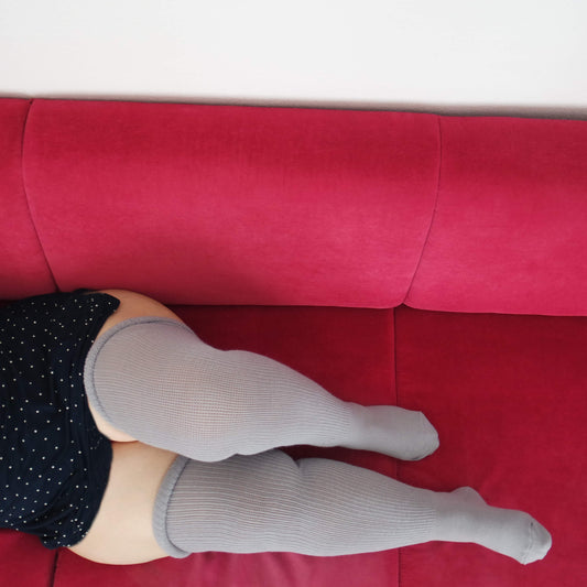A woman wears plus size extra long thigh high stocking. She lay down on red couch with Warm air gray extra wide opening knit thigh high sock style makes her cozy.